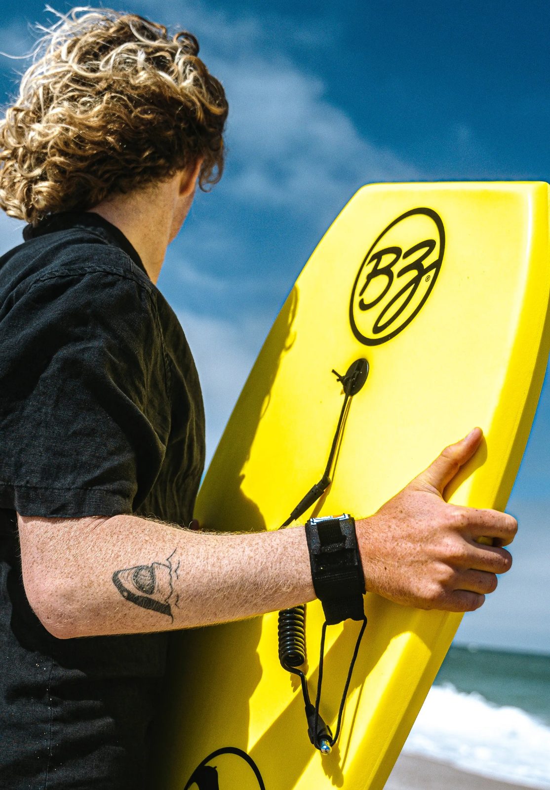 Bodyboarder carrying a yellow BZ board at the beach